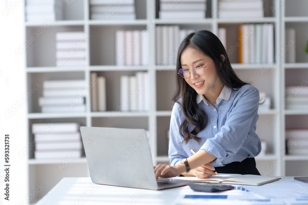 Happy young Asian businesswoman sitting at desk and take notes with laptop computer in the office. Happy young Asian businesswoman sitting at desk and take notes with laptop computer in the office.