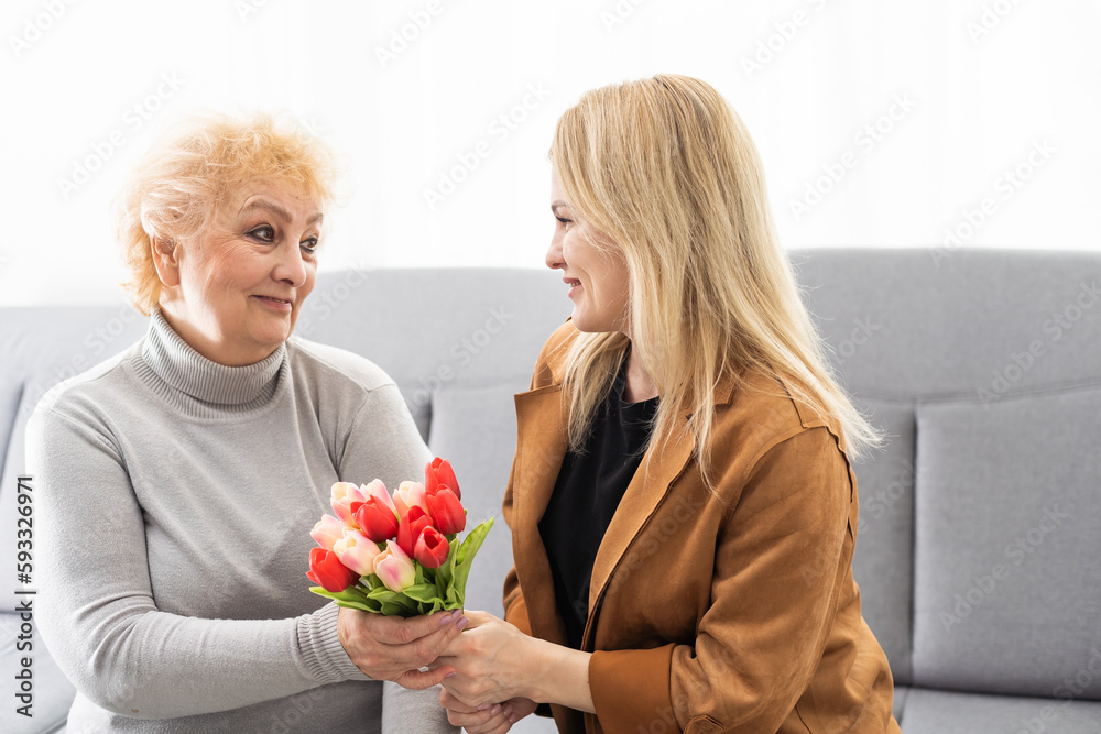 Happy mother's day. Beautiful young woman and her mother with flowers at home.
