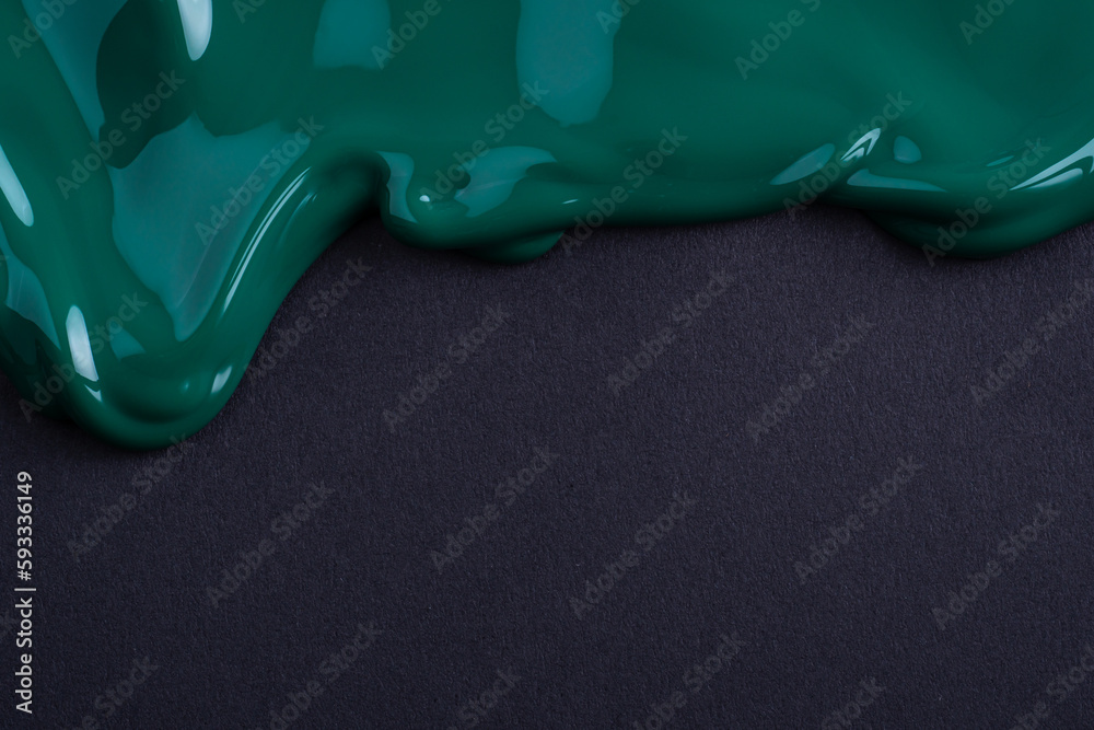 Dark green liquid drops of paint color flow down on black paper