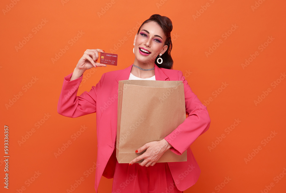 happy smile girl holding shopping bags and showing credit card while looking at camera isolated over orange background happy smile girl holding shopping bags and showing credit card while looking at camera isolated over orange background