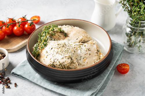Baked chicken fillet in a creamy sauce with thyme in a bowl on a light background with fresh vegetables and herbs. The concept of healthy diet homemade food