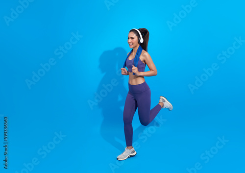 young asian fitness woman in sportwear running wearing headphones listening to music isolated on blue copy space studio background . excited runner © NaMong Productions