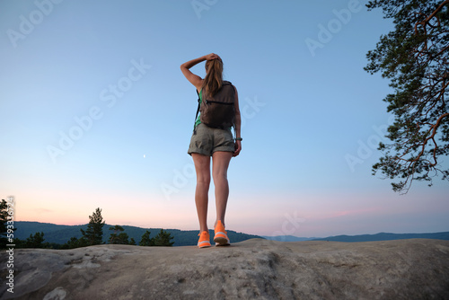 Fototapeta Naklejka Na Ścianę i Meble -  Young woman hiker standing alone on mountain footpath enjoying view of evening nature on wilderness trail. Active way of life concept