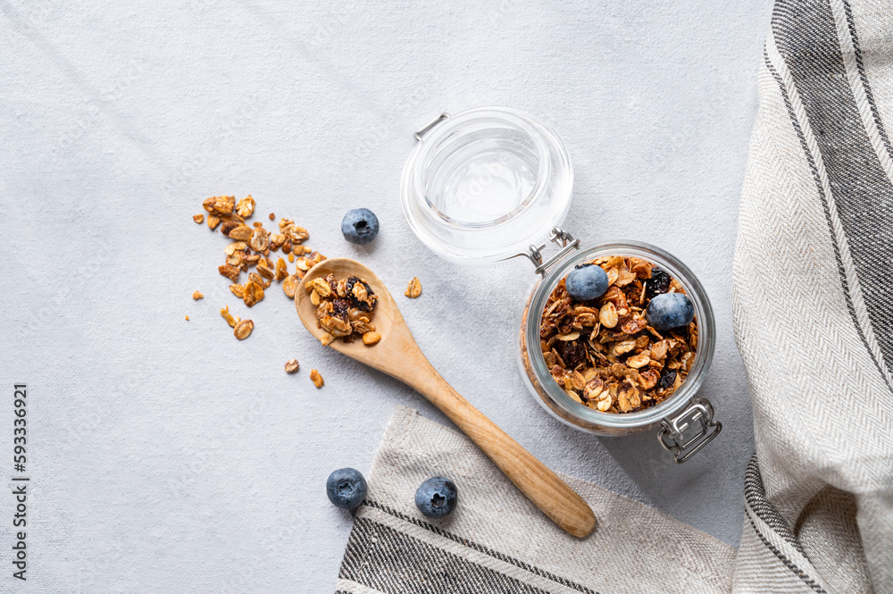 Fototapeta premium Homemade baked granola with nuts and fresh blueberry in a jar on a light background. Healthy vegetarian muesli for breakfast.