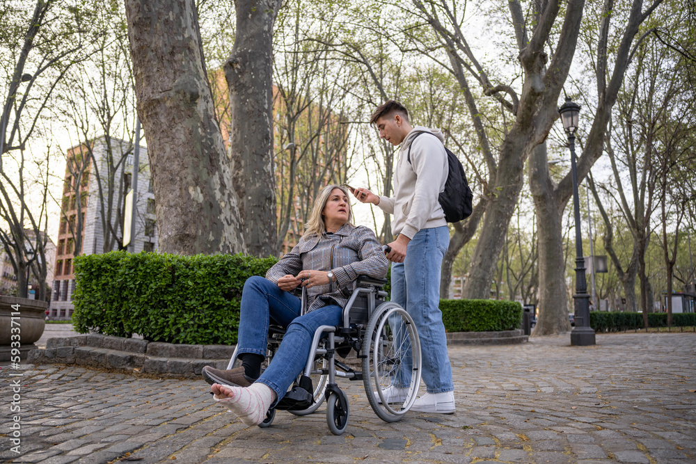 Teenager looking at mobile phone while carrying her mother in a wheelchair. Teenager looking at mobile phone while carrying her mother in a wheelchair.