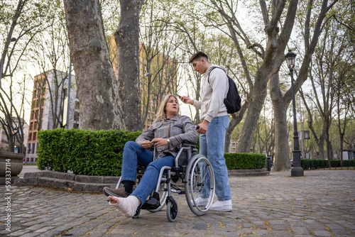 Teenager looking at mobile phone while carrying her mother in a wheelchair.