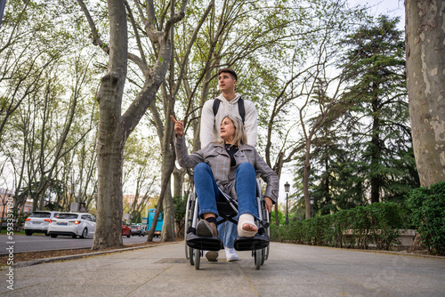 A teenage son carrying his mother in a wheelchair.