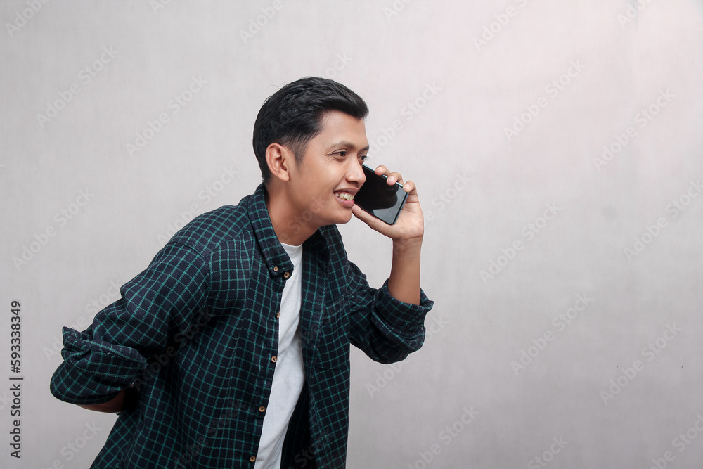 Asian mature man in plaid shirt taking his cell phone, talking, body hunched over with happy face Asian mature man in plaid shirt taking his cell phone, talking, body hunched over with happy face