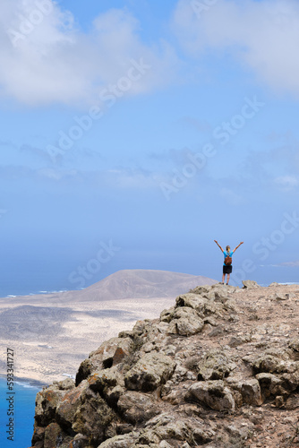 Woman with arms raised on top of a hill. With La Graciosa Island in the background