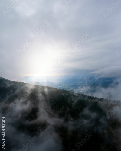 Drone vertical shot of fog over mountains with sunrays