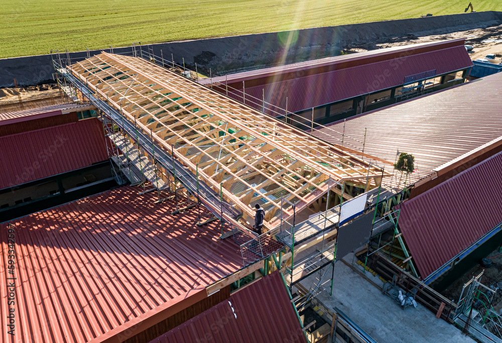 Naklejka premium Luftbild-Nahaufnahme einer im Bau befindlichen Tierwohl - Schweinemastanlage,Holzkonstruktion für den zentralen Zuluftkanal auf dem neu eingedeckten Dachflächen.