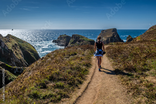 Young Woman On Coastal Hiking Path With Spectacular Cliffs At Peninsula Pointe Du Van On Cap Sizun At The Finistere Atlantic Coast In Brittany, France
