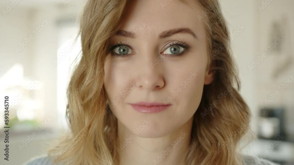 Close up of face of cute young serious woman with short blond hair and expressive eyes. Minimum of make-up and styled hair. Blurry background of apartment. High quality 4k footage Close up of face of cute young serious woman with short blond hair and expressive eyes. Minimum of make-up and styled hair. Blurry background of apartment. High quality 4k footage