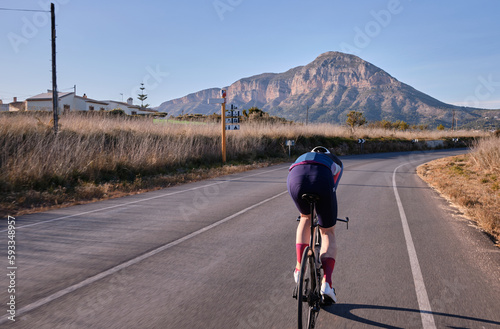 Fit cyclist on time trial aero bike riding his bike in aero position towards the mountains on empty road. Sport trainings approach that deliver results through hard work and dedication.