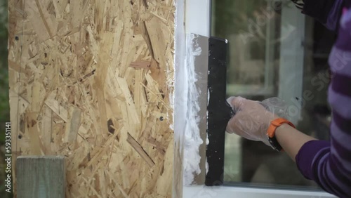 Woman worker paints slopes of windows of her own wooden house. Hand with brush
