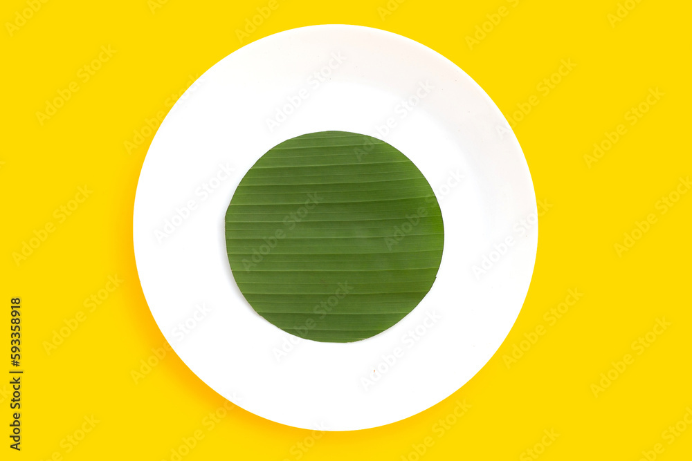 Cut banana leaves into circle shape on plate on yellow background. Cut banana leaves into circle shape on plate on yellow background.