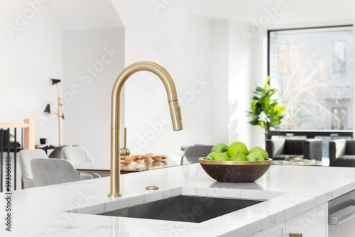Canvas Print A gold kitchen faucet detail with a white marble countertop, white cabinets, and decorations in the background