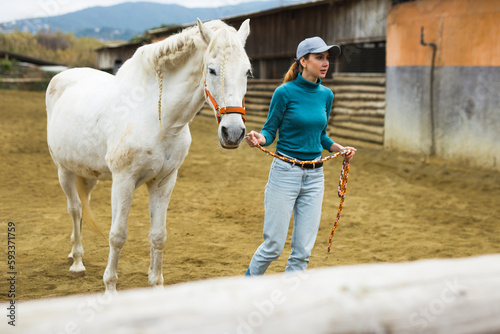 Female jockey walking a white horse in paddock