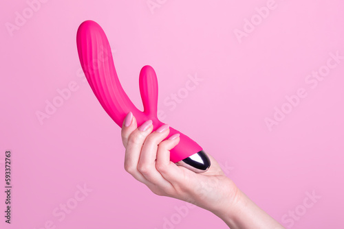Pink sex toy rabbit shaped vibrator for women in female hand isolated on light pink background photo