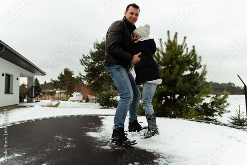 dad and daughter jump on a trampoline that stands on the street in the winter season, have fun together. © Vadym