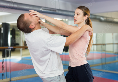 Caucasian woman grabbing man's face while sparring with him in gym during self-defence training.