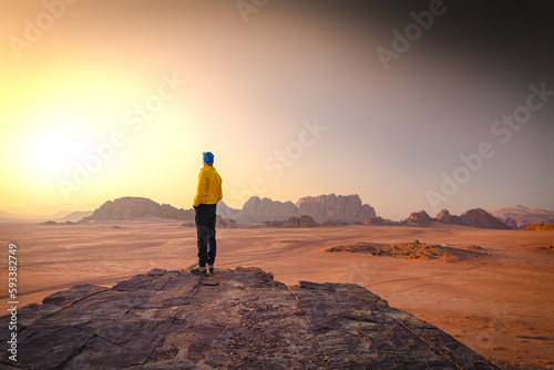 Wadi Rum w Jordanii. Mężczyzna stojący na pustynnej formacji skalnej patrzący na wschód słońca. 