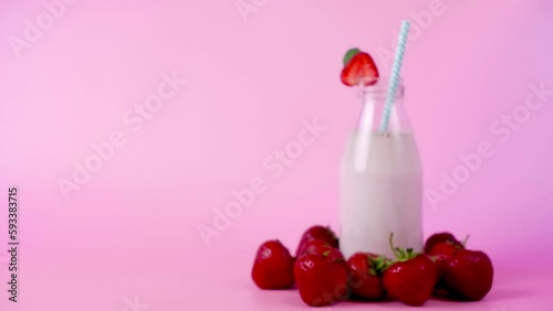 Out of focus strawberry smoothie or milkshake in glass bottle moving on pink background and slowly coming into focus