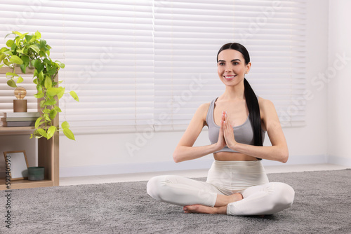 Woman in sportswear meditating at home, space for text