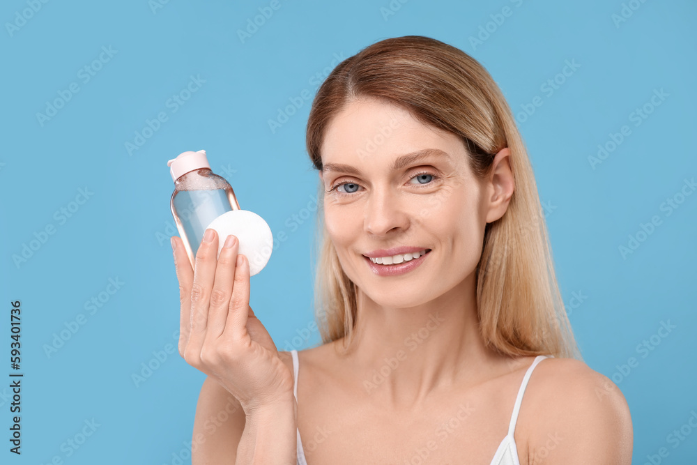 Beautiful woman with makeup remover and cotton pad on light blue background Beautiful woman with makeup remover and cotton pad on light blue background