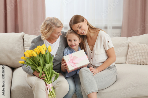 Little girl congratulating her mom and granny with flowers and gift at home. Happy Mother's Day