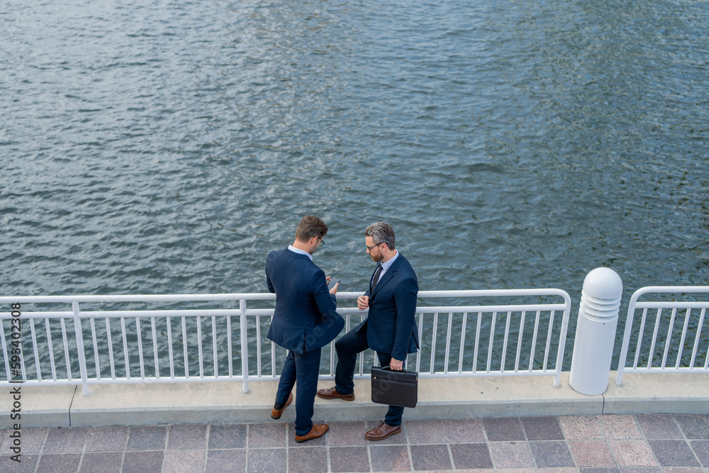 Outdoor business meeting. Photo of business partners talk conversation outdoor. Two handsome businessmen in suits discuss a working project against the background of urban city.