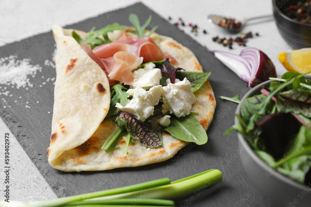 Delicious pita wrap with jamon, cheese cream and greens on light gray table, closeup