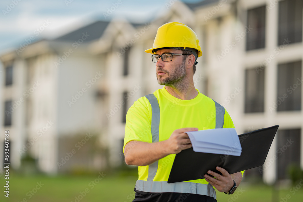 Fototapeta premium Engineer with clipboard, building inspection. Builder at construction site. Buider with helmet on construction outdoor. Worker at construction site. Bilder in hardhat.