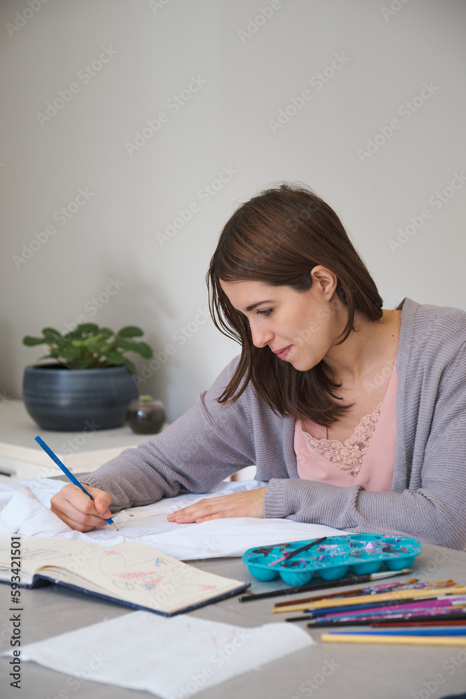 Caucasian woman painting a design in a white shirt. Woman's creative expression through painted clothing designs. Caucasian woman painting a design in a white shirt. Woman's creative expression through painted clothing designs.