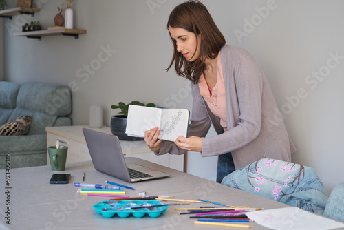Caucasian influencer woman showing her sketchbook to her community in a stream. Unique clothing designs.