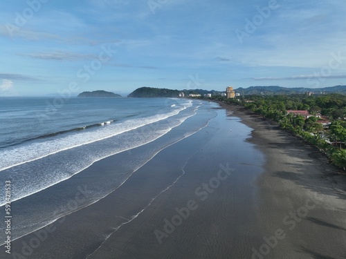 Jaco Beach, a popular surfing destination in Costa Rica, is captured in stunning aerial shots from a drone, showcasing its long sandy shore, waves, palm trees, and colorful beachfront buildings. © WildPhotography.com