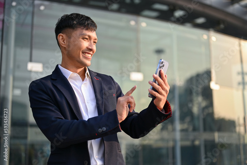 Happy Asian businessman using his smartphone while standing outside of the company building.