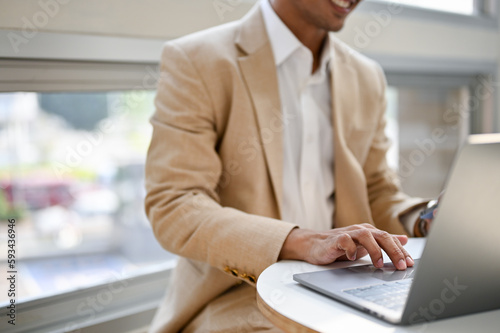 Close-up image of an Asian businessman remote working at a cafe, using his laptop.