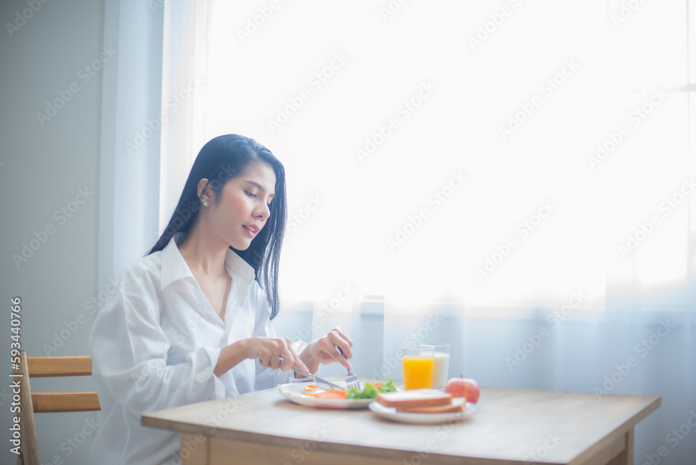 Beautiful asian woman is eagerly slicing a fried egg on a plate with a desire. Beautiful asian woman is eagerly slicing a fried egg on a plate with a desire.