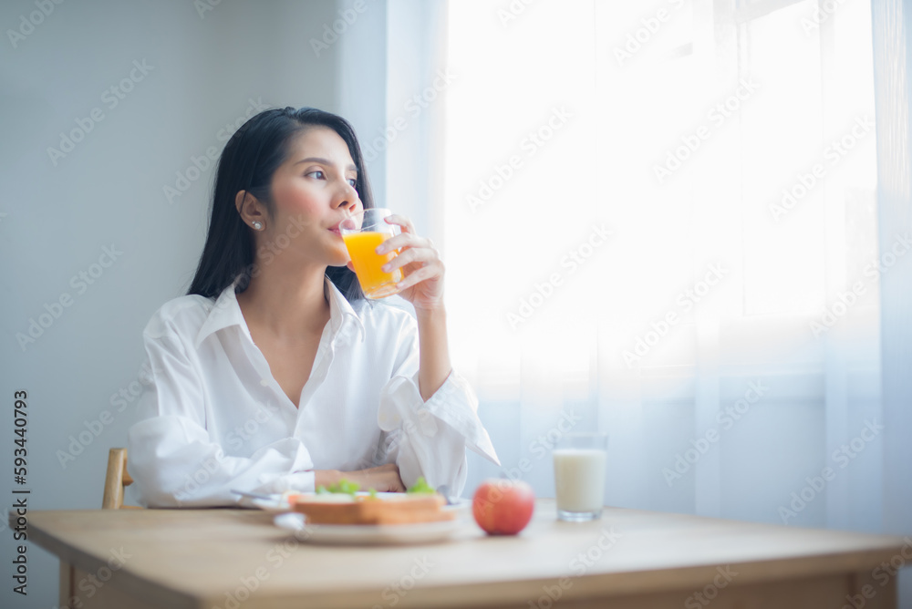 Beautiful asian woman savored her glass of juice while gazing into the copy space with breakfast on the table. Beautiful asian woman savored her glass of juice while gazing into the copy space with breakfast on the table.