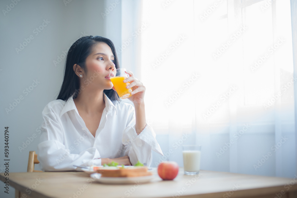 Beautiful asian woman drinking juice while looking to the copy space with breakfast on the table. Beautiful asian woman drinking juice while looking to the copy space with breakfast on the table.