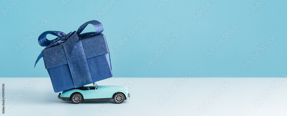 small Luxury gift box with a blue bow on on top of retro toy car. Side view monochrome. Fathers day or Valentines day gift for him. Corporate gift concept or birthday party. Festive sale delivery - obrazy, fototapety, plakaty 