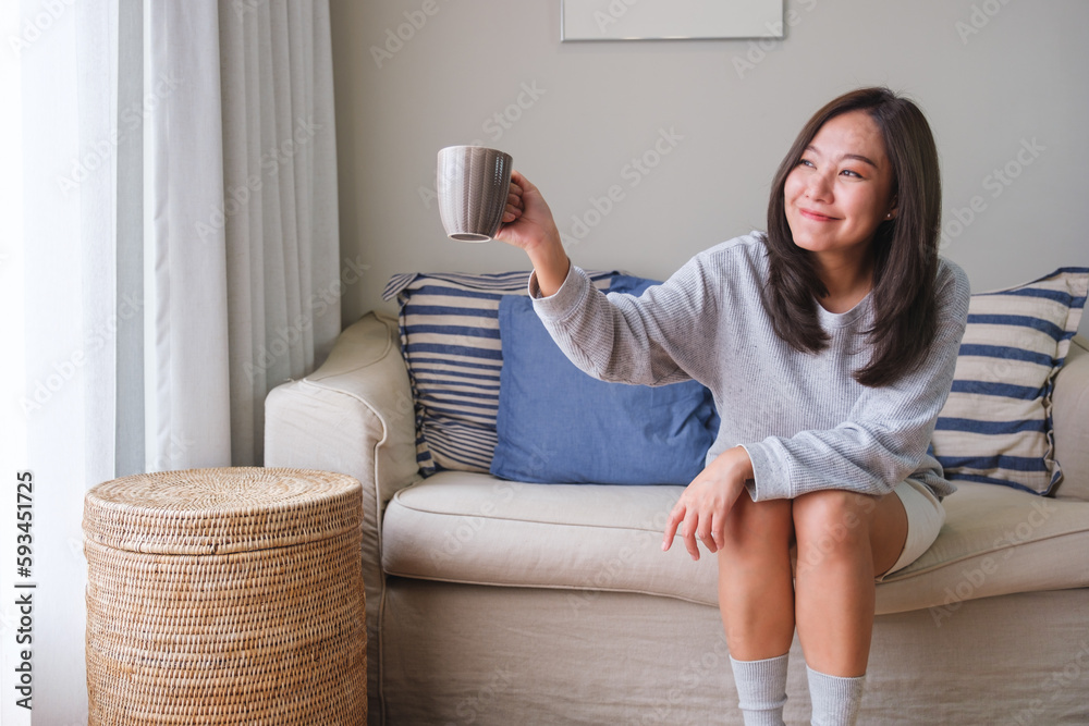Fototapeta premium Portrait image of a young woman raising hand and say hi to friends outside while drinking coffee at home