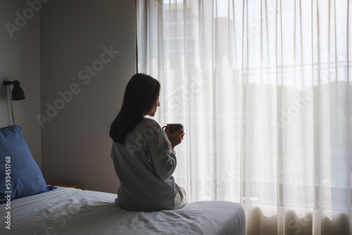 A young woman drinking hot coffee after waking up in bedroom