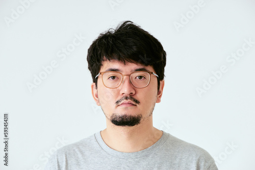 白背景で眼鏡をかけた髭を生やしたカメラ目線の30代の1人の日本人男性の人物の上半身の正面