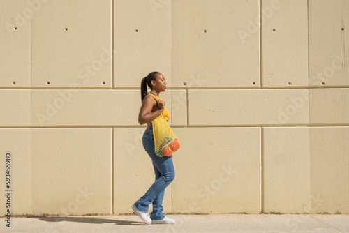 profile african american woman in colored clothes walking with cloth shopping bag
