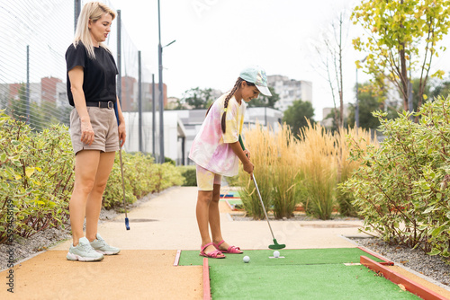 Obraz na płótnie mother and daughter playing mini golf, children enjoying summer vacation