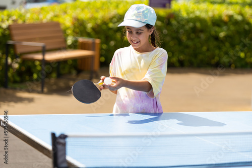 Young teenager girl playing ping pong. She holds a ball and a racket in her hands. Playing table tennis outdoors in the yard. © Angelov