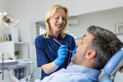 Young female dentist examining teeth of her patient during appointment at dental clinic. Hands of a doctor holding dental instruments near patient's mouth. Healthy teeth and medicine concept