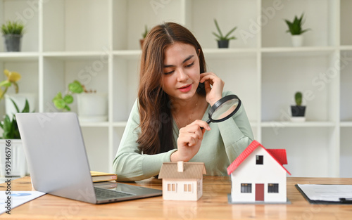 Caucasian female appraiser hold magnifying glass examining house model, checking assessment of dwelling. Concept of real estate appraisal, property, land valuation, house search. photo
